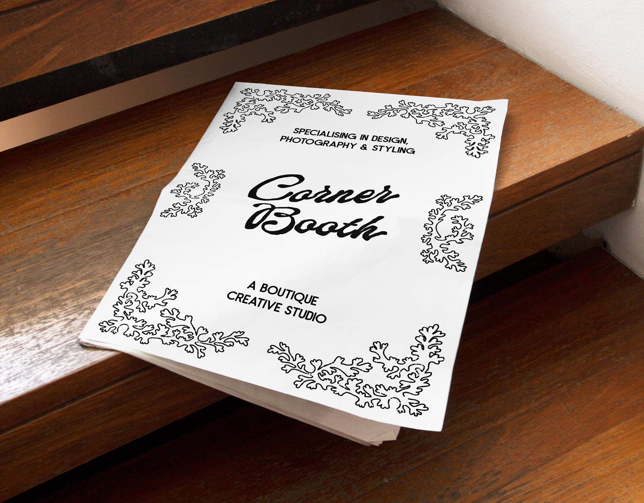 A mockup displaying a physical magazine lying on wooden stairs, the design reads "Corner Booth: a boutique creative studio specializing in design, photography & styling"