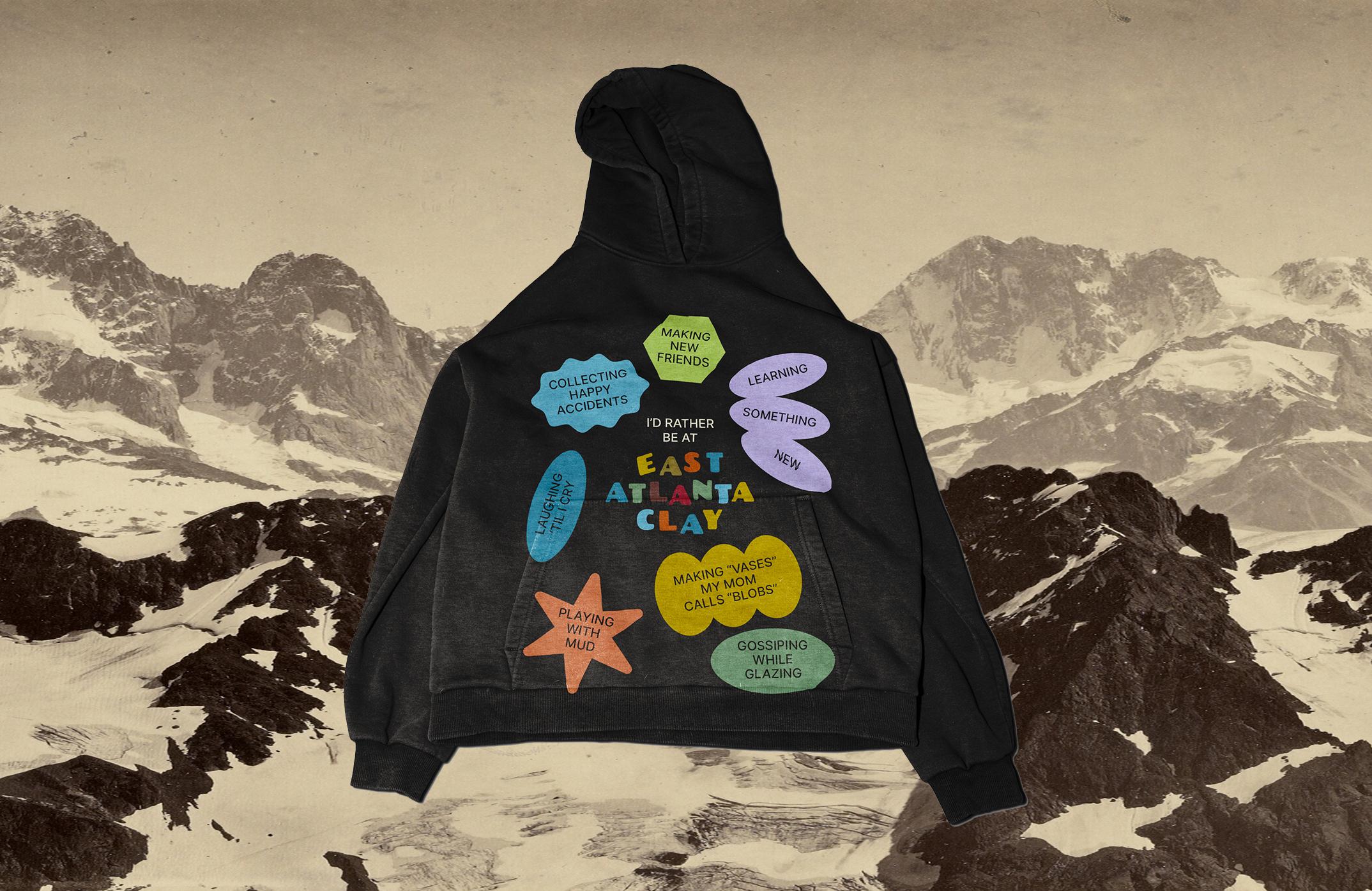 A hoodie mockup with a very playful, colourful design reading "I'd rather be at East Atlanta Clay... collecting happy accidents, making new friends, learning something new, laughing 'til I cry, making "vases" my mom calls blobs, playing with mud, gossiping while glazing"