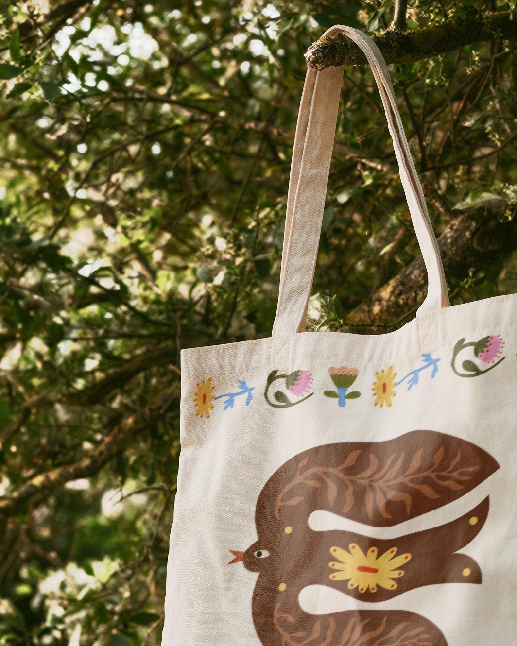 Close-up of a tote bag decorated with custom illustrated flowers and folklore-ish birds